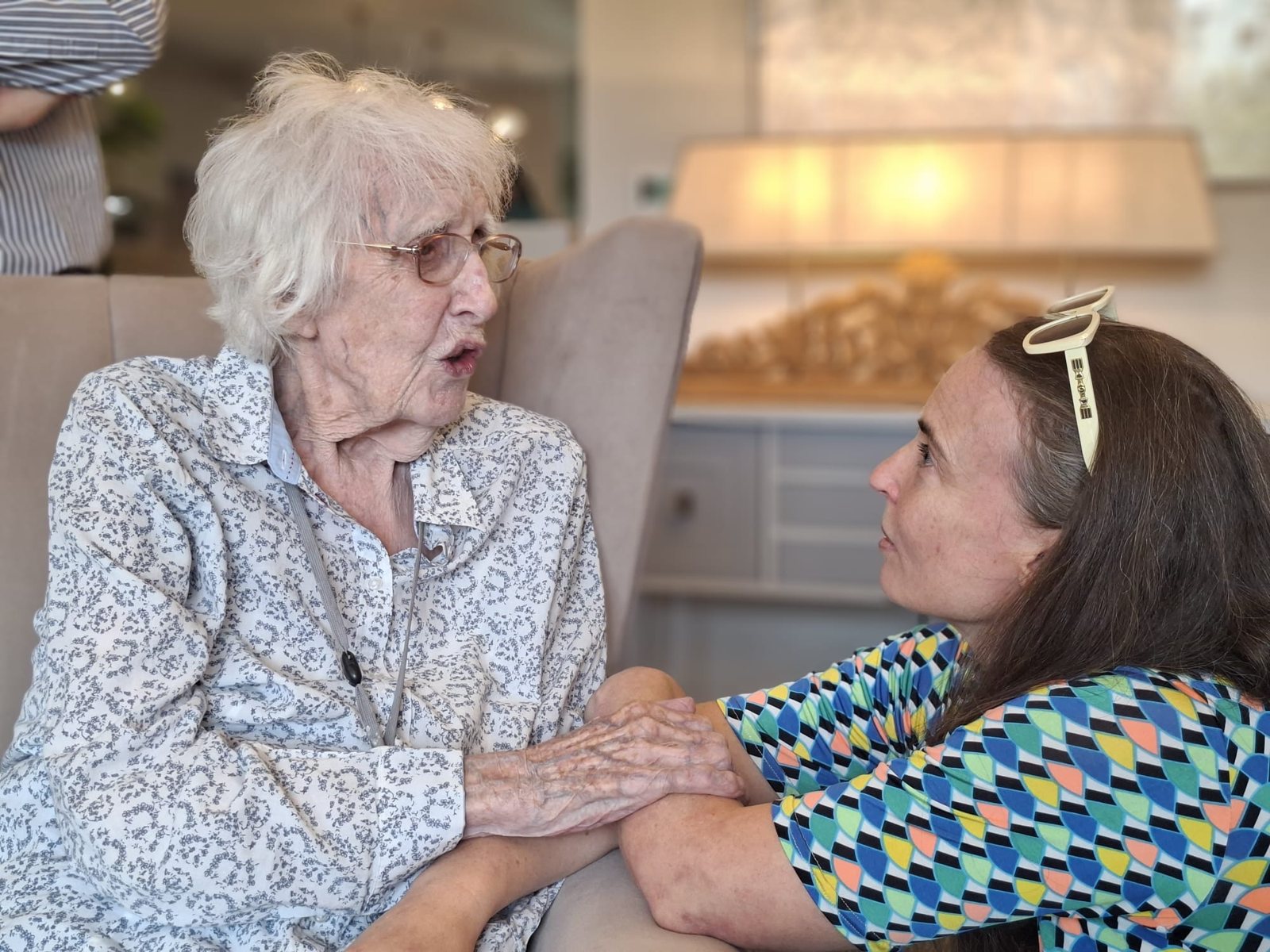 Ruth, 101, in her armchair, holding hands with her granddaughter Tara